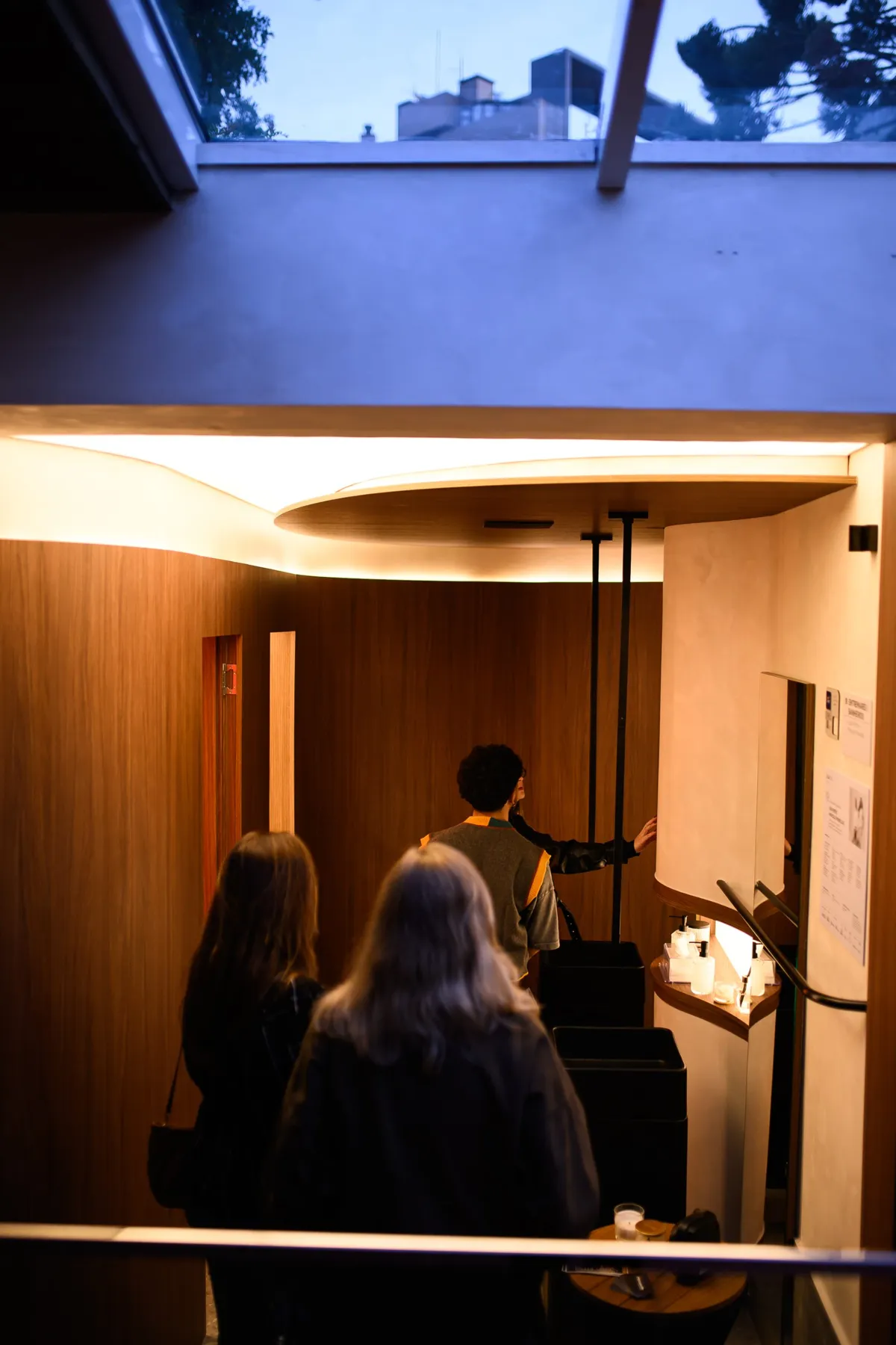 EntreMarés ao entardecer, com visitantes no hall de madeira curva e forro iluminado